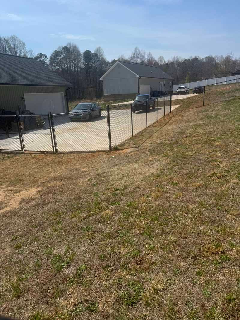 Grassy slope beside a fenced driveway and house under a clear blue sky