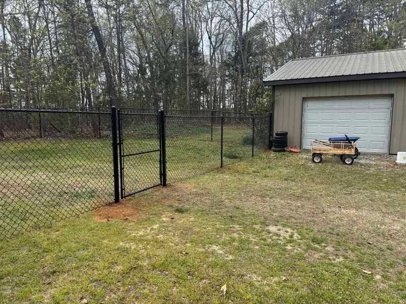 Chain-link fence beside a garage in a grassy yard with trees in the background