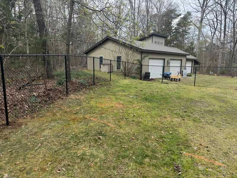 Small beige house with garage beside a fenced grassy yard and woods in a cloudy setting