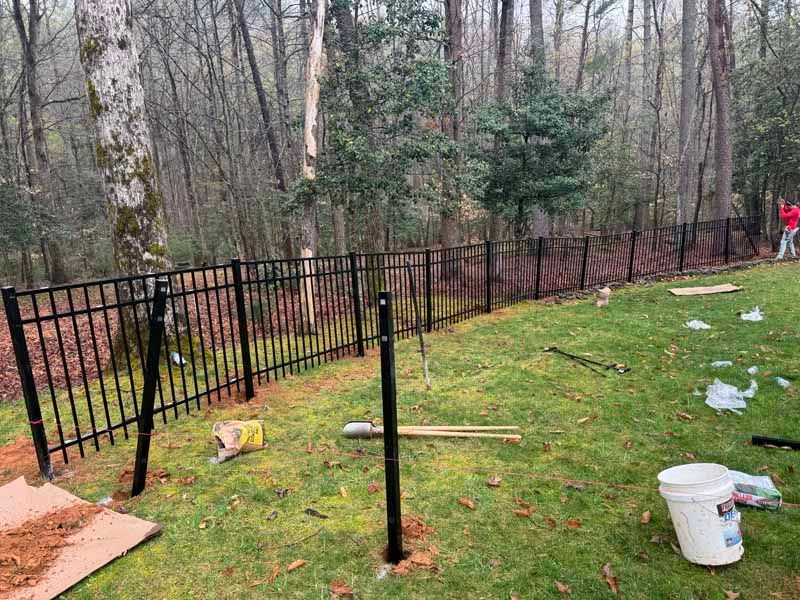 Black metal fence being installed along a grassy yard with tools and buckets scattered nearby.