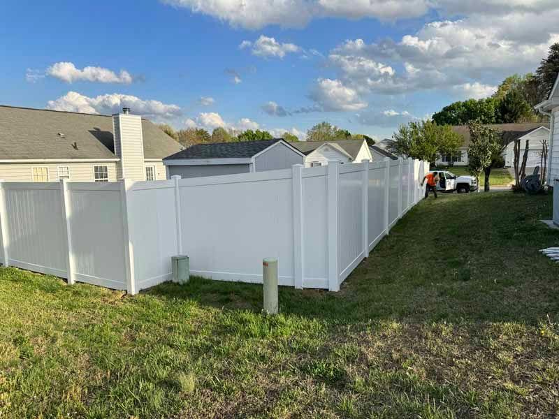 White vinyl fence around a backyard beside houses under a blue, cloudy sky