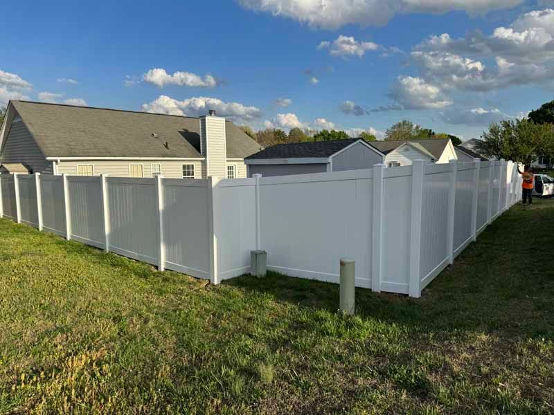 White vinyl fence enclosing a yard beside a house under a blue sky