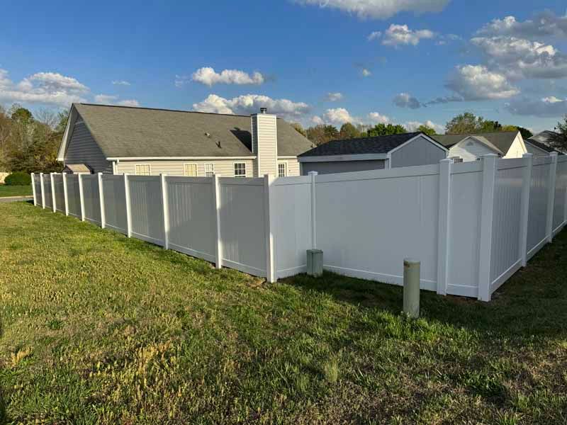 White vinyl fence around a suburban yard beside a house under a blue sky