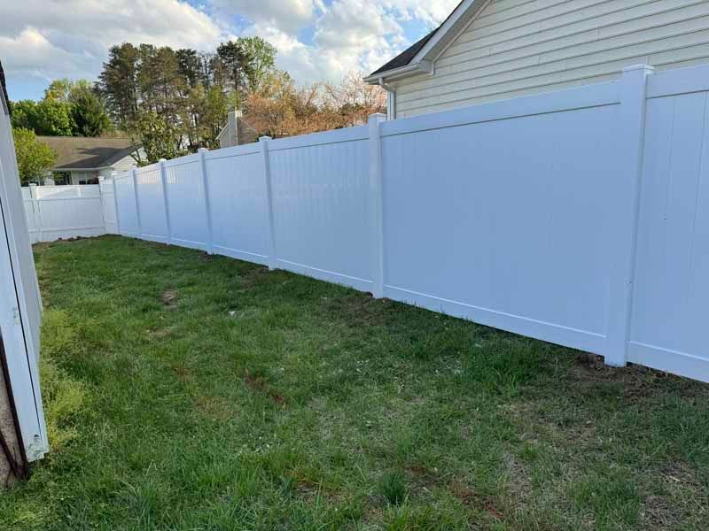 White vinyl fence along a grassy yard beside a house under a partly cloudy sky
