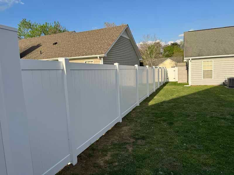 White vinyl fence along a grassy side yard between beige houses under a clear sky