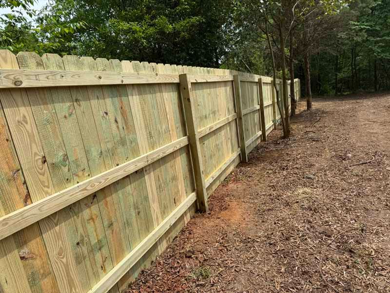 Wooden privacy fence along a leaf-covered yard beside a wooded path