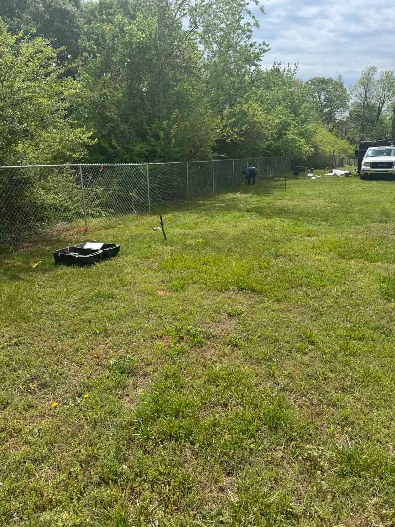 Grassy yard with chain-link fence, trees, and a parked white SUV in the distance.