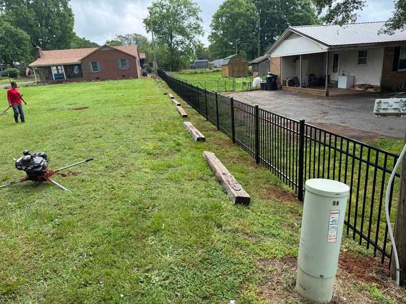 Backyard with new black fence, wooden rails, grassy yard, and workers near a house after heavy rain