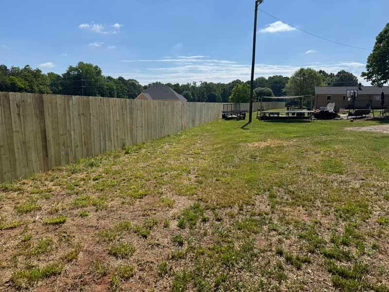 Grassy backyard with a wooden fence, utility pole, and a deck near a house under a blue sky
