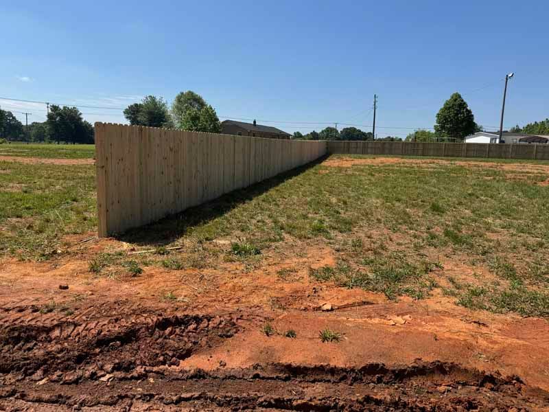Long wooden fence along a grassy, mostly bare lot under a clear blue sky.