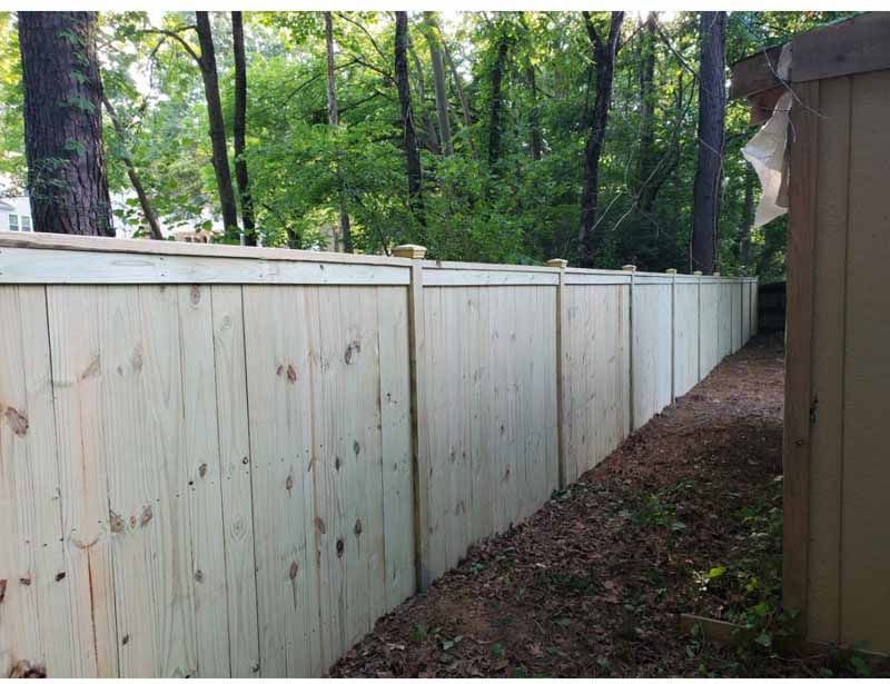 Wooden privacy fence along a narrow wooded backyard path beside a house