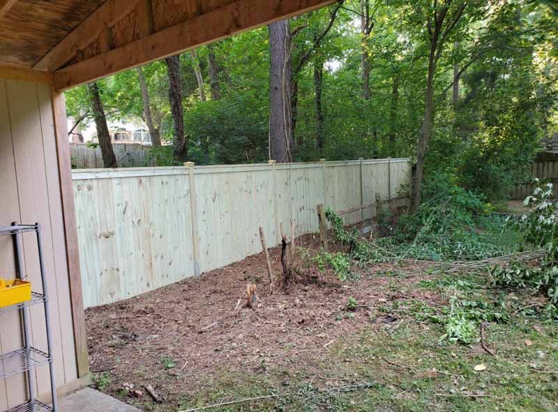 Backyard with a new light wood fence, trees, and a dirt patch under a covered patio