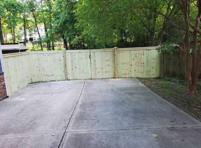 Concrete driveway leading to a cream wooden fence with trees and greenery behind it