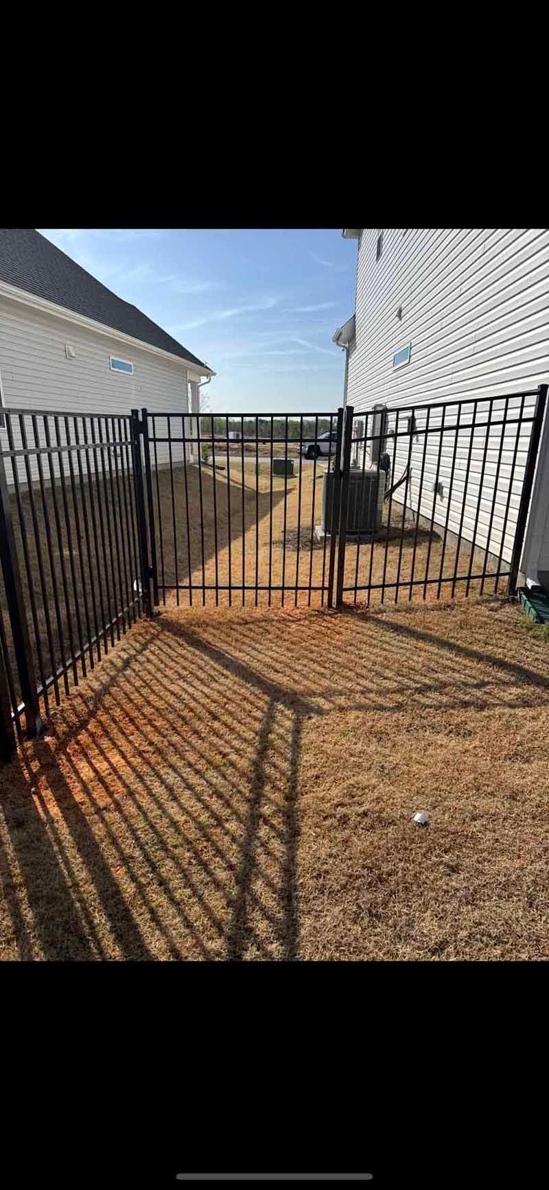 Black metal gate in a narrow gravel walkway between two white buildings under a blue sky.