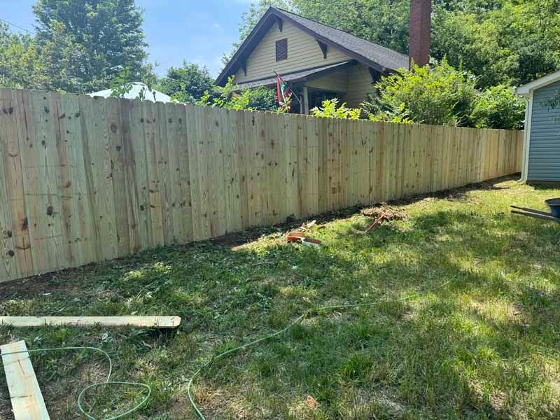 Backyard with wooden privacy fence, grassy lawn, and a house behind it.