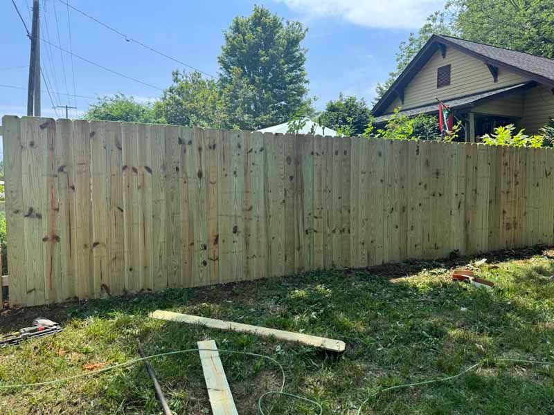 Wooden privacy fence in a grassy yard with a house and trees in the background