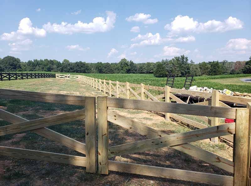 Wooden farm gate and fenced pasture under a blue sky with clouds