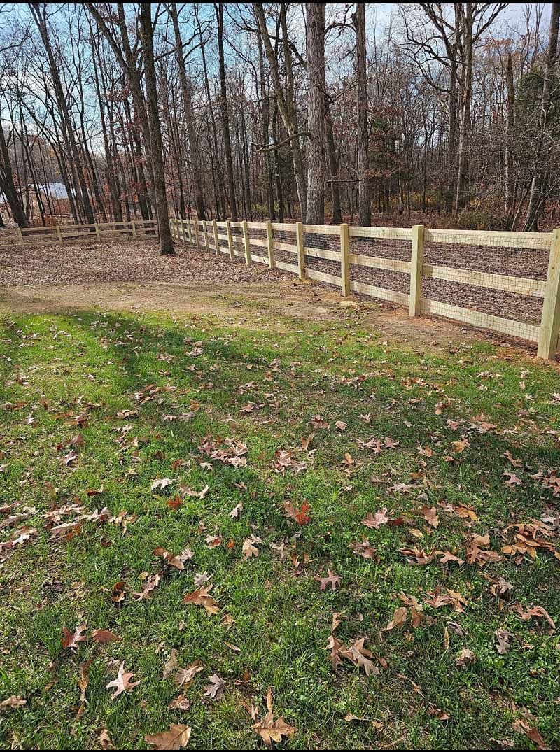 Wooden fence along a leaf-covered grassy field beside bare trees in late fall