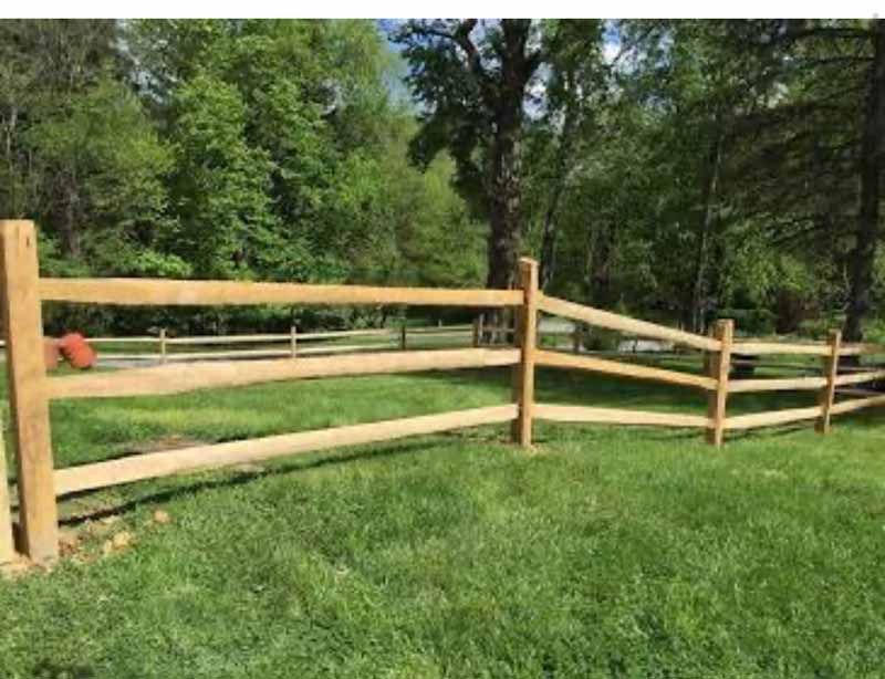Wooden split-rail fence bordering a green grassy yard with trees in the background