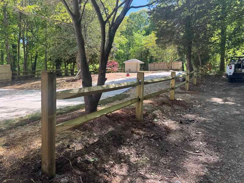 Wooden fence beside a dirt path along a tree-lined road in a wooded area