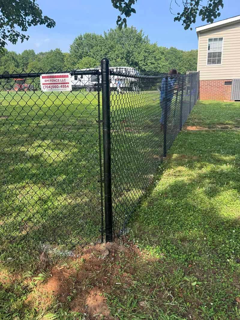 Black chain-link fence corner in a grassy yard with a beige building and red sign in the background