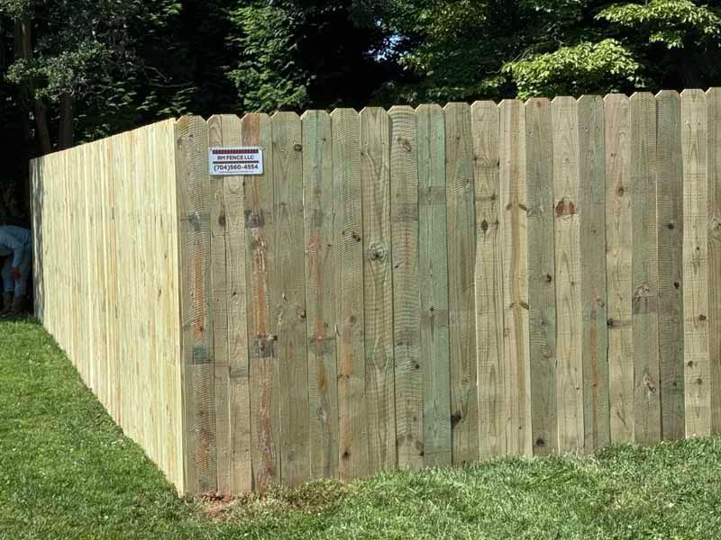 Wooden backyard fence with a small posted sign, bordering a grassy lawn and trees.