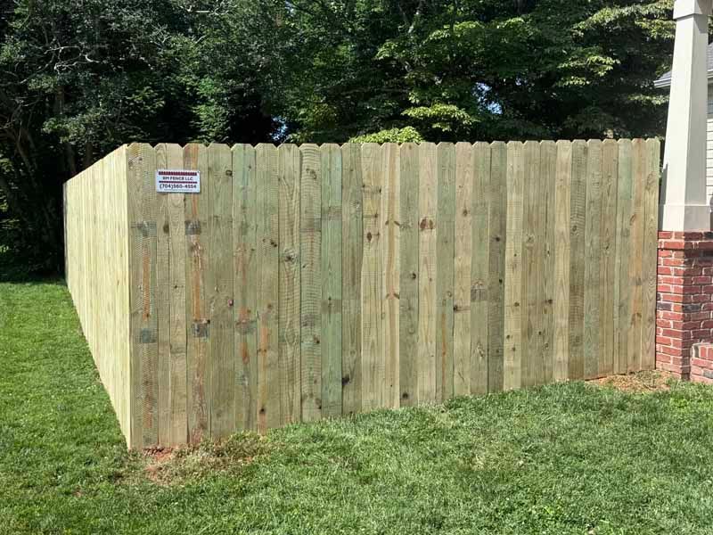 Wooden privacy fence beside a grassy yard, with trees and a brick house corner visible.