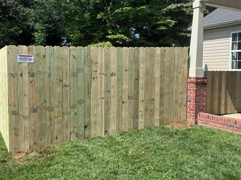 Wooden privacy fence beside a house with a red brick porch and grassy yard