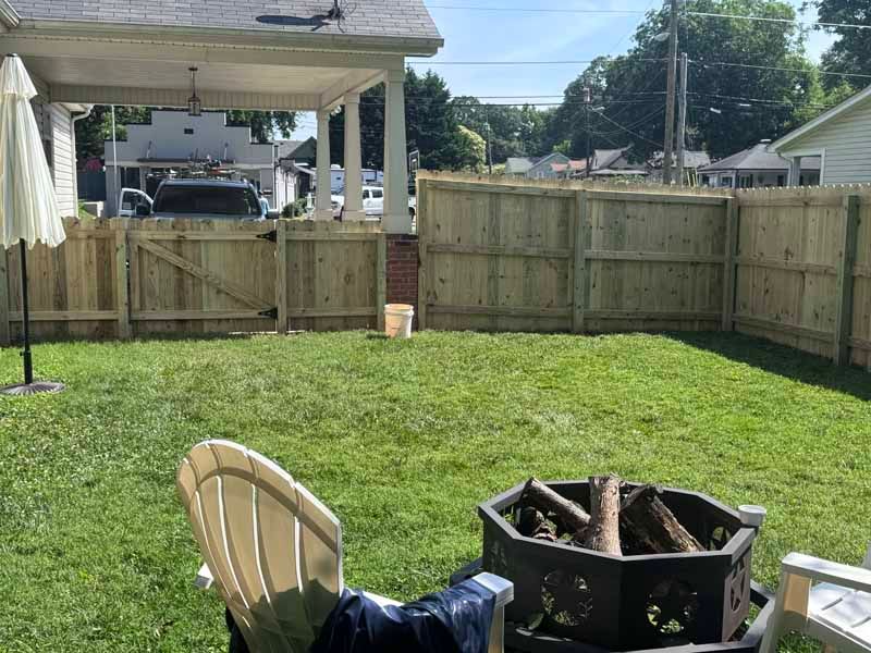 Backyard lawn with a fire pit, folding chair, and wooden fence under a covered patio