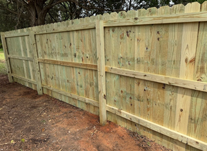 New wooden privacy fence along a muddy yard with trees in the background