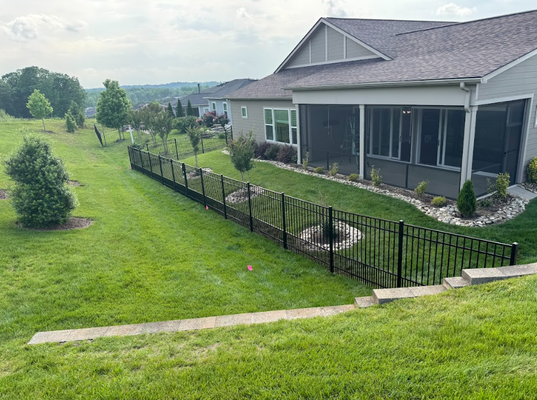 Suburban backyard with green lawn, black fence, and screened porch on a house overlooking a distant landscape