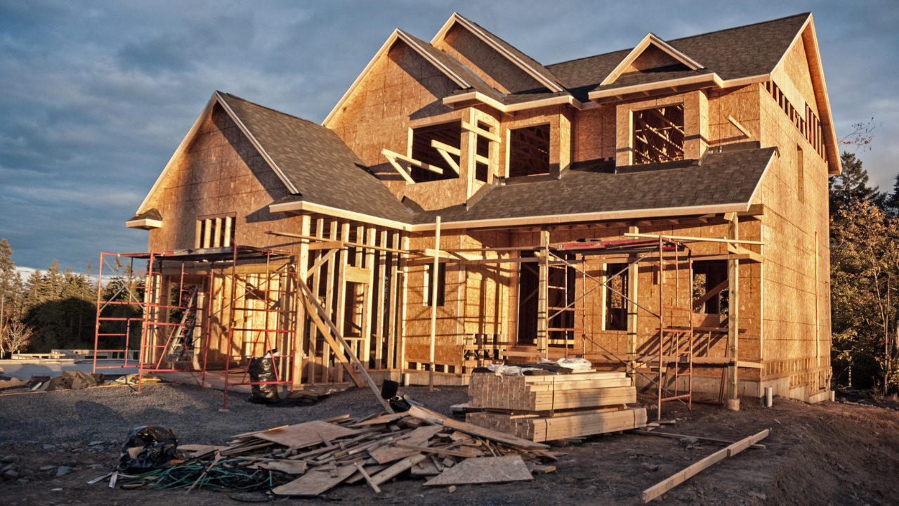 House under construction, wooden frame visible, unfinished exterior, and scattered building materials.