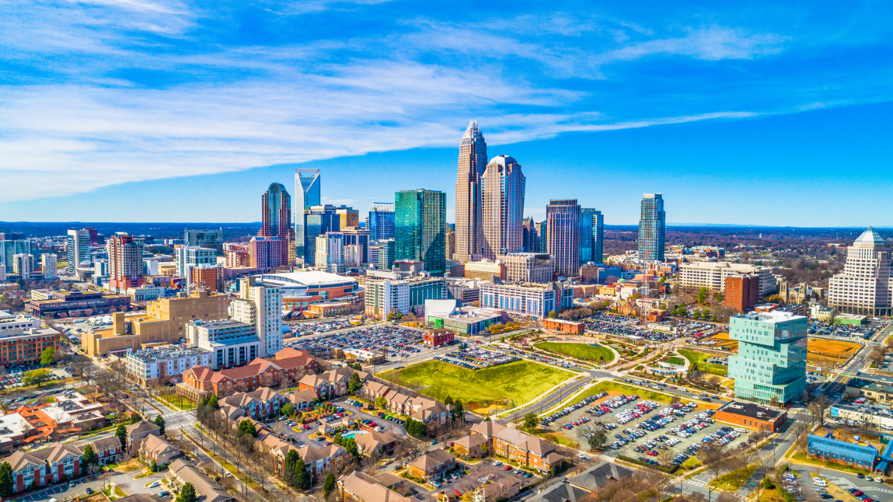 Charlotte, NC skyline with blue sky, modern buildings, and green spaces.