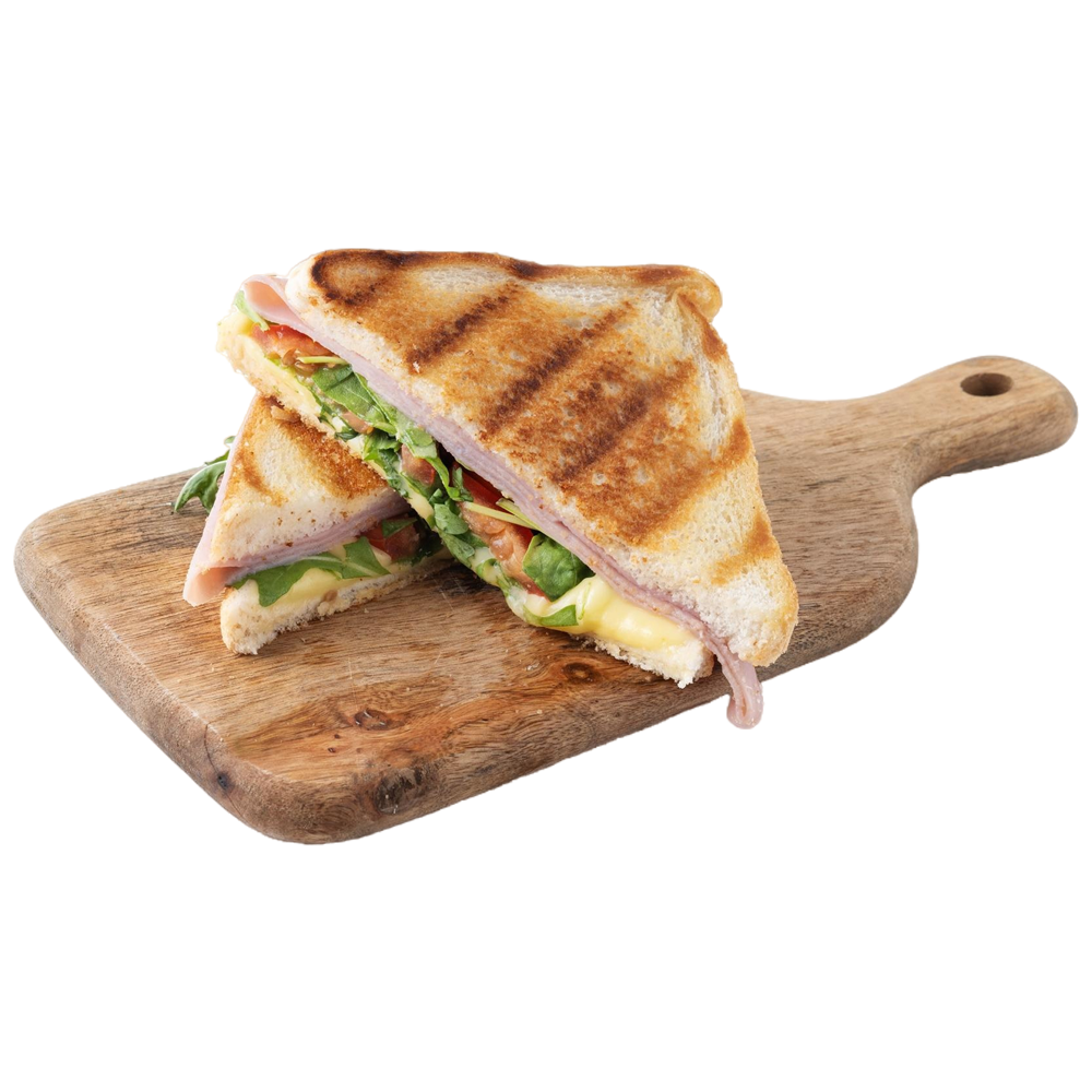 Toasted sandwich, cut in half, on a wooden cutting board, with ham, cheese, and greens visible.