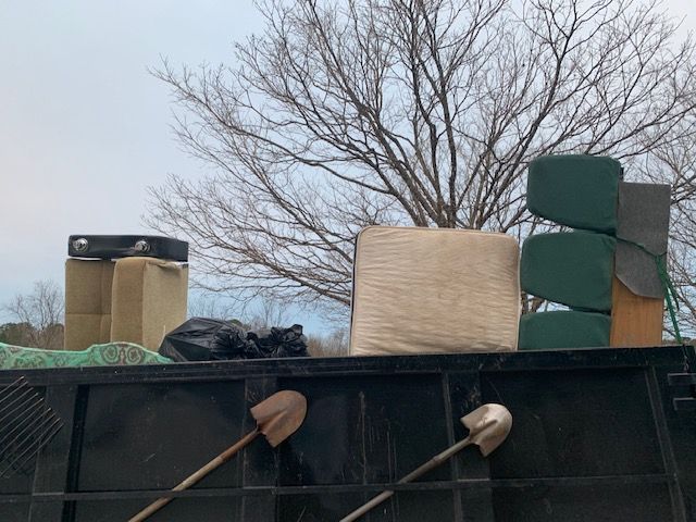 A dumpster filled with boxes and shovels with a tree in the background