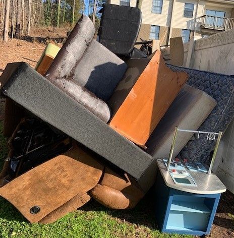 A pile of furniture is sitting on the grass in front of a house.