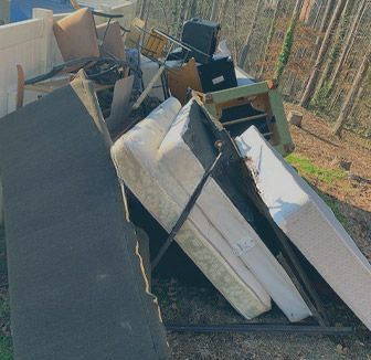 A pile of wooden chairs , tables , and other furniture in front of a brick building.