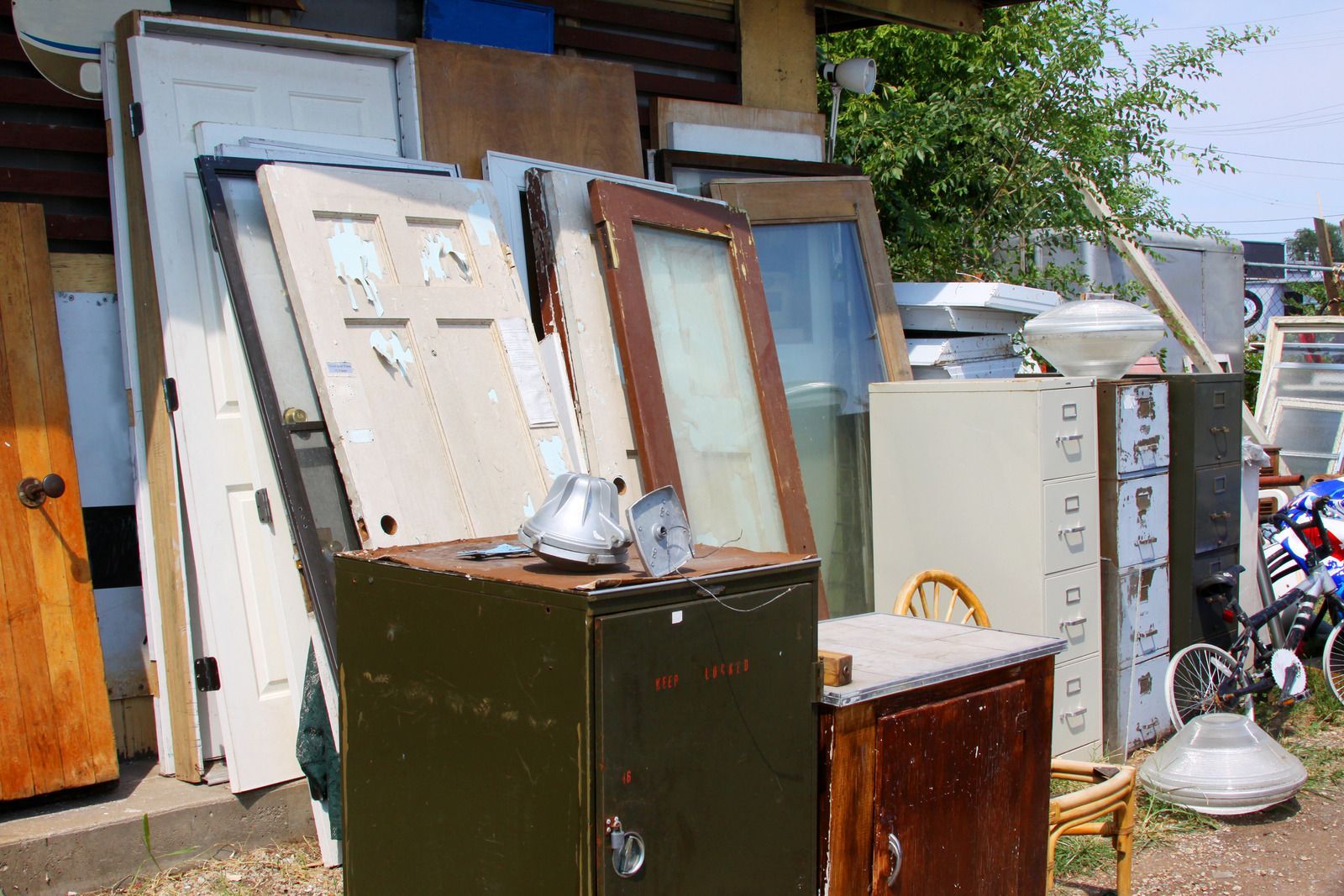 Pile of discarded doors, cabinets, and household items stacked outdoors in a cluttered area.