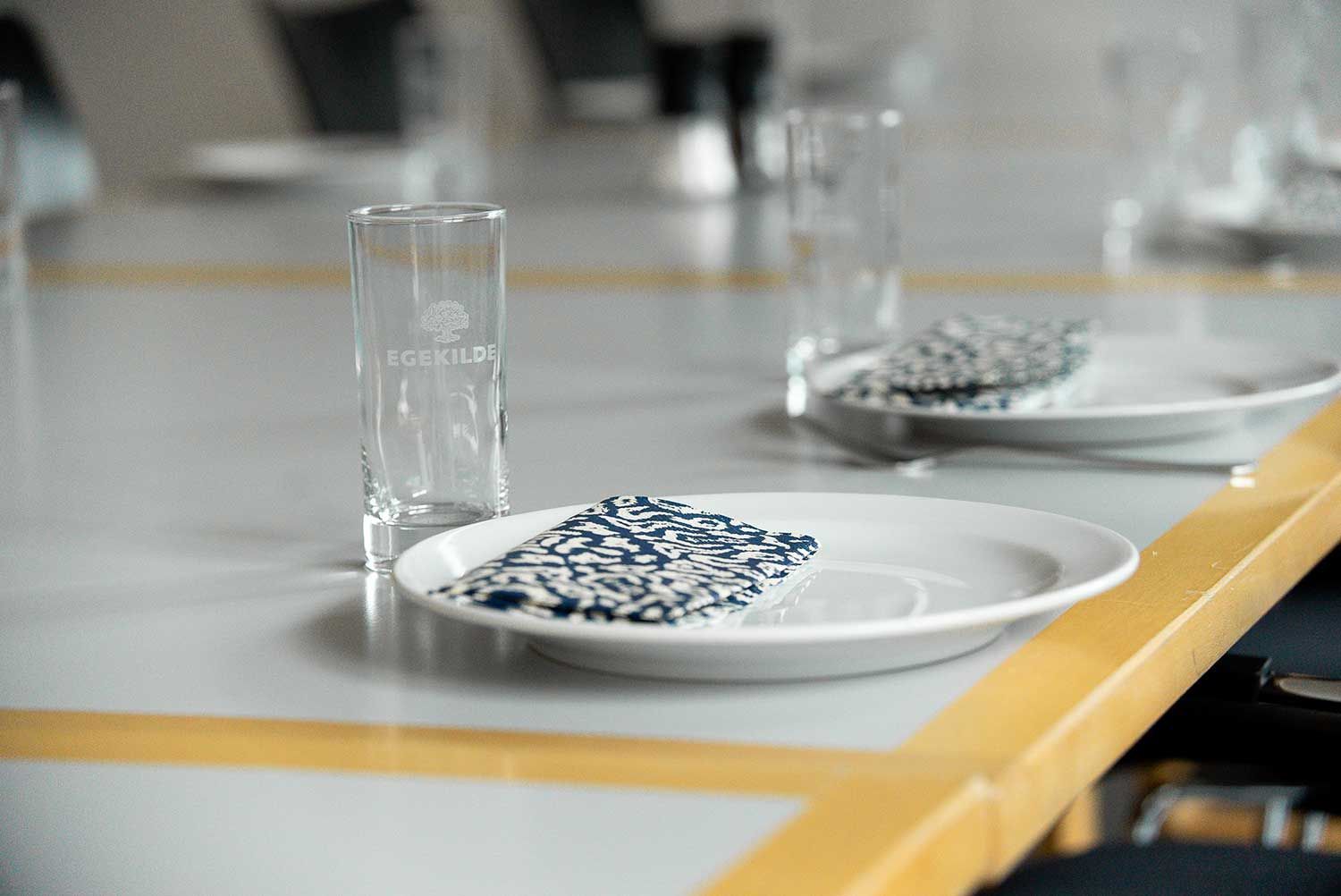 En borddækning med et glas, en tallerken og en serviet med blå pletter.