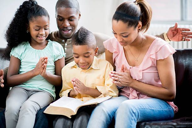 A family is sitting on a couch reading the bible together.