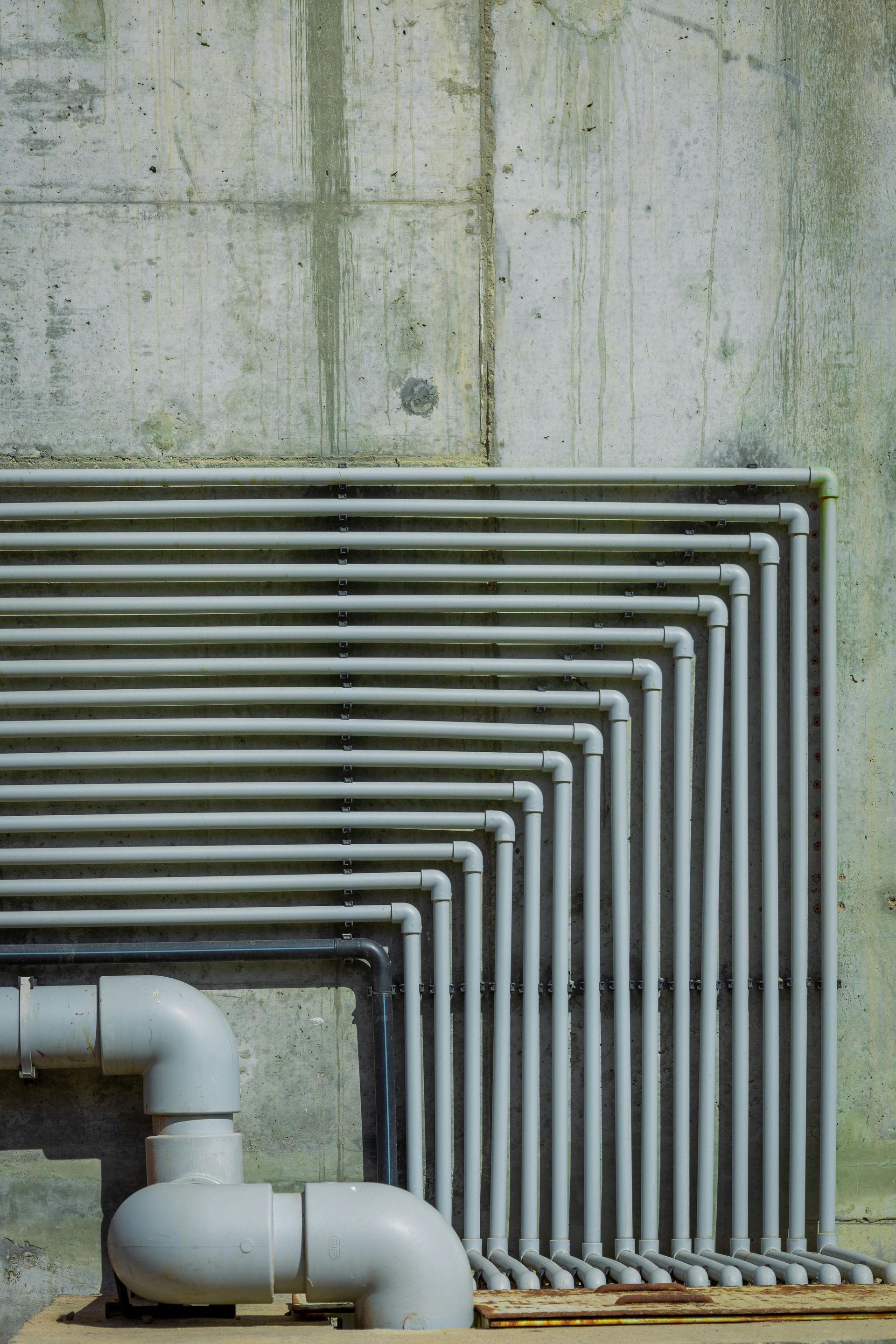 Gray pipes run along a concrete wall, turning sharply at the corner.