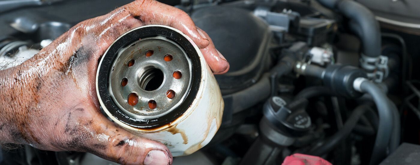 A person is holding a dirty oil filter in front of a car engine.