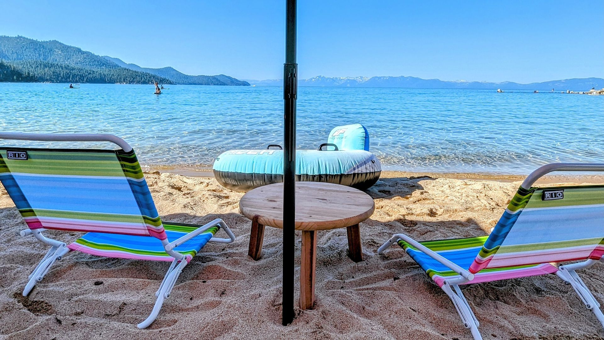 Beach chairs and a table under an umbrella beside Lake Tahoe