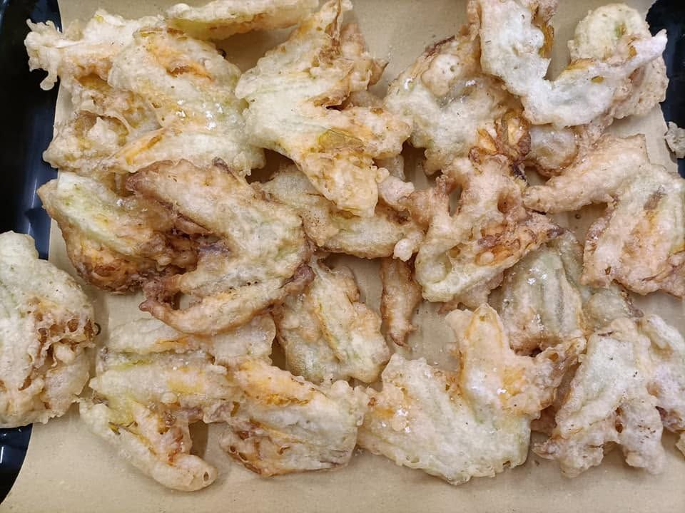 Pezzi di pollo fritto ammucchiati su un vassoio, ricoperti di pastella dorata e salsa