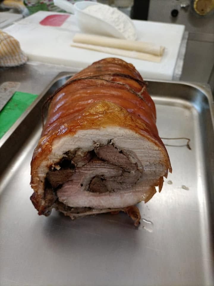 Rotolo di maiale arrosto con cotenna croccante su una teglia metallica in un’area di preparazione della cucina