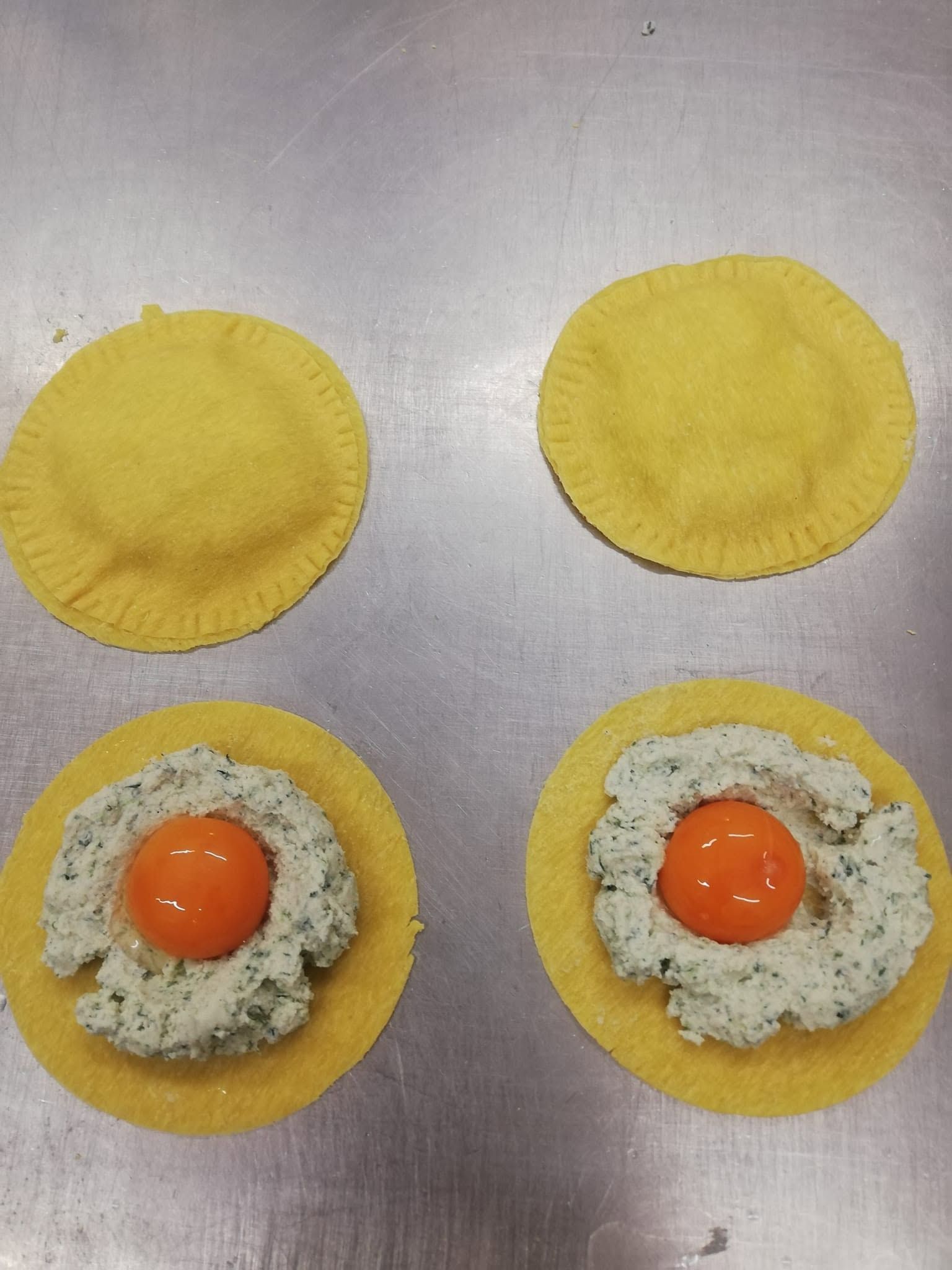 Quattro gusci rotondi di pasta gialla, due farciti con un composto cremoso e tuorli arancioni, su una superficie argentata