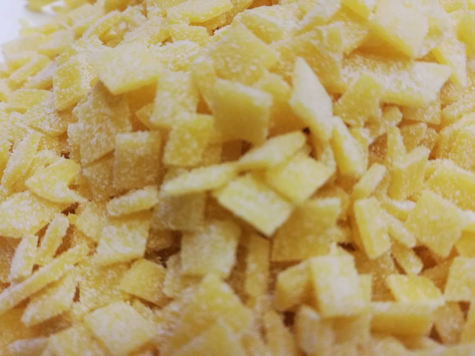 Primo piano di piccoli pezzi gialli tagliati a dadini, probabilmente ingredienti alimentari, ammassati insieme