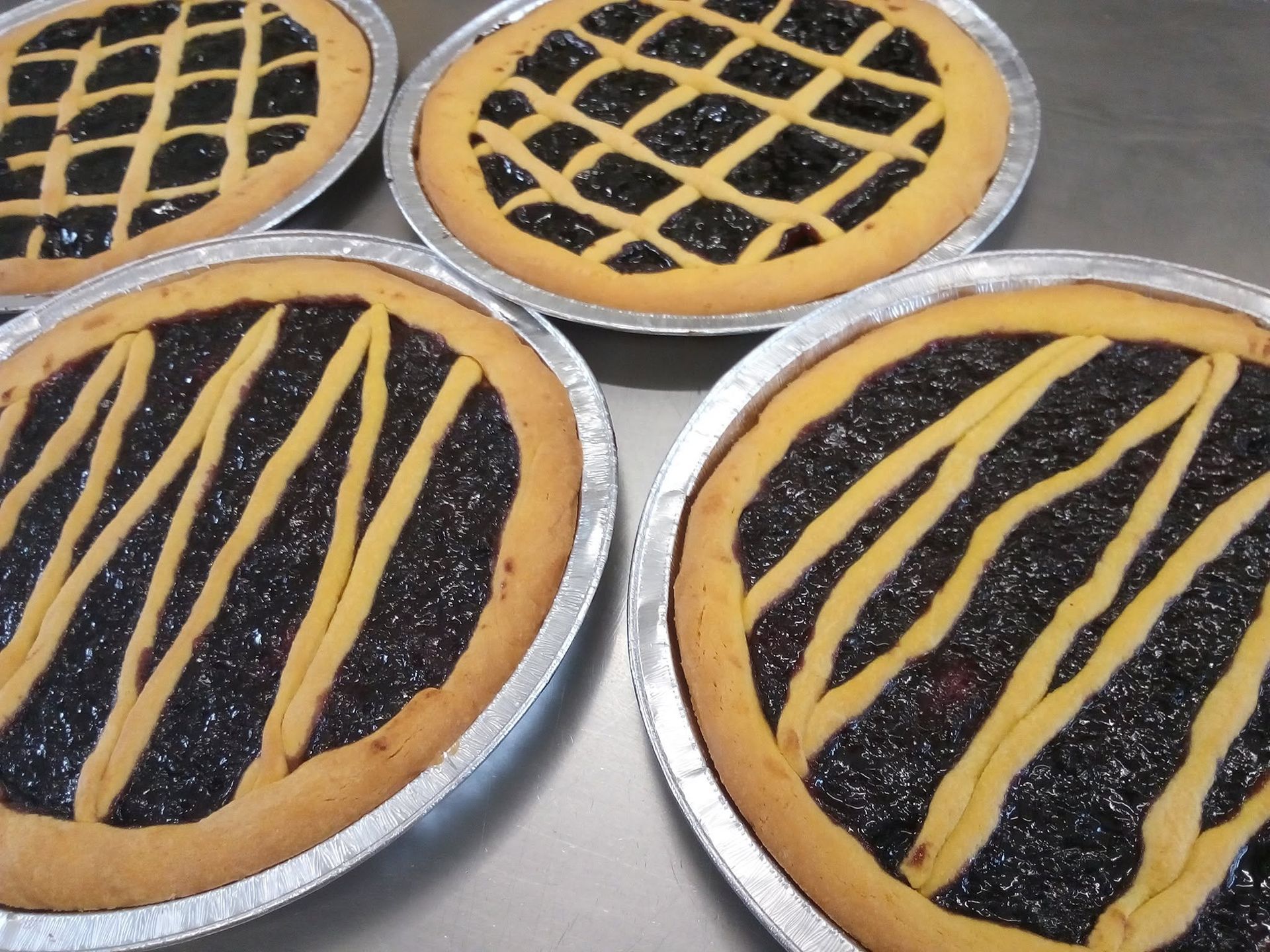 Quattro crostate alla frutta con la superficie a grata e a strisce, in teglie metalliche su un piano di lavoro