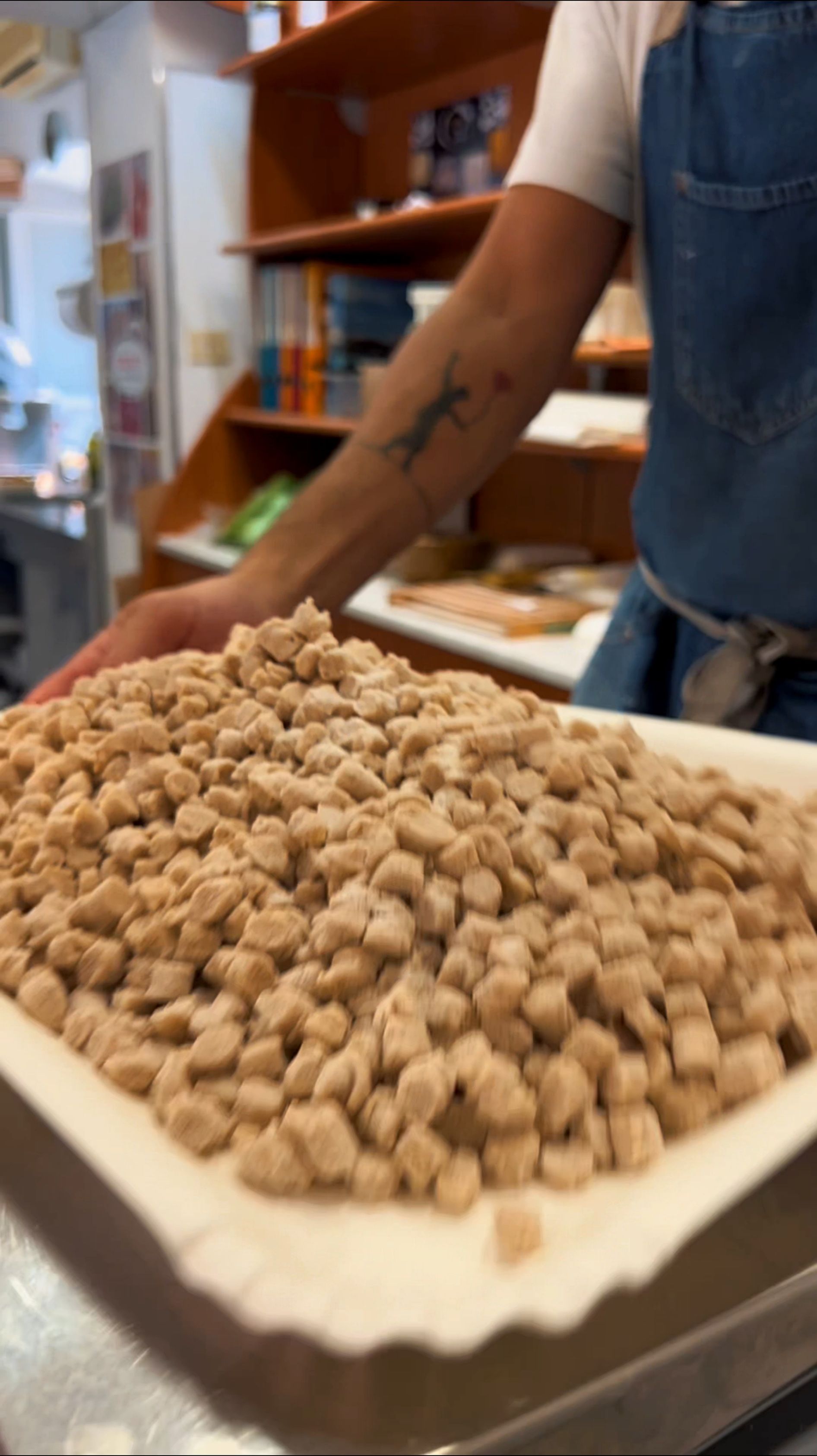 Vassoio con piccoli croccantini beige sul bancone, accanto a una persona con il grembiule in un negozio