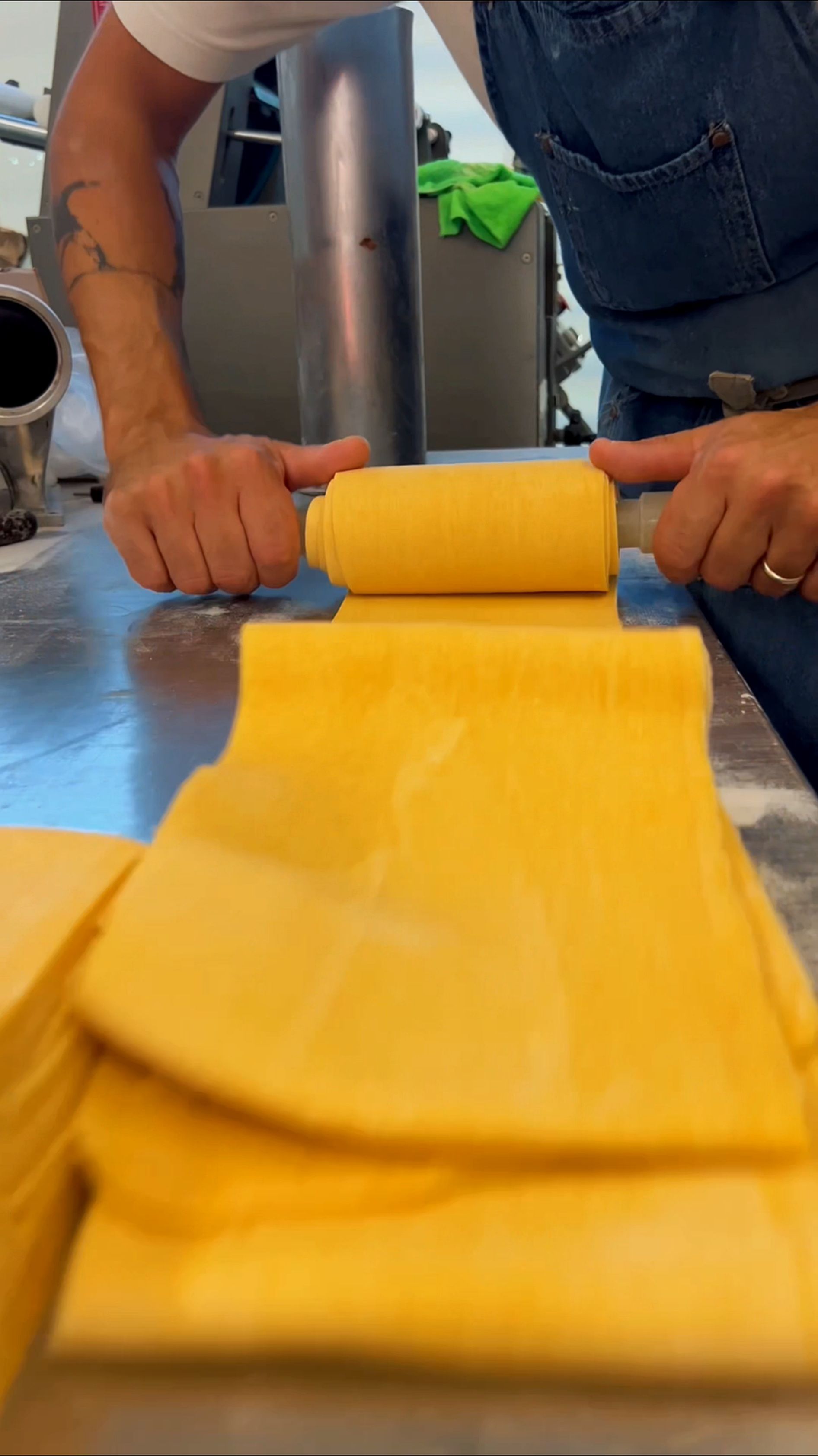 Mani che stendono un impasto giallo brillante con il mattarello su un piano di lavoro blu.